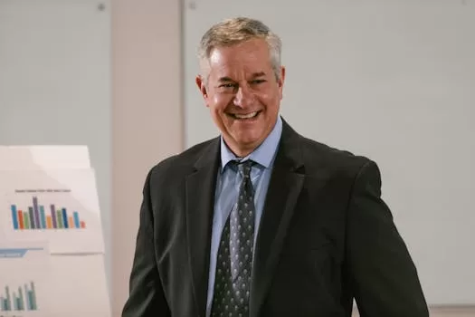 Smiling businessman in a corporate setting with charts. Professional and confident.